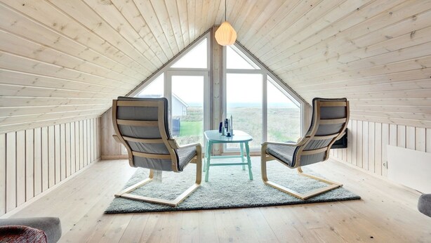 Una habitación con techo inclinado, dos sillas, una mesita y vistas amplias por un gran ventanal.
