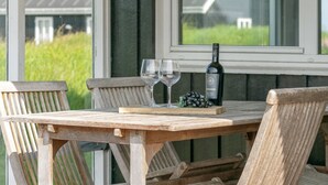 Una mesa de madera con dos copas de vino y una botella, frente a una ventana que da a un paisaje verde.