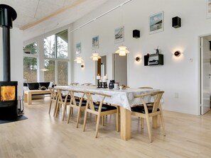 Moderni ruokailutila, jossa on pitkä puinen pöytä, tuoleja ja puukamina.