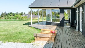 Et moderne hus med en overdækket terrasse, en træterrasse og en græsplæne.