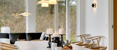 Comedor con una mesa dispuesta para cuatro personas, que incluye un mantel blanco, sillas de madera y un centro de mesa con velas.