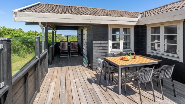 A wooden deck with a table and chairs, a covered seating area, and a view of the ocean.