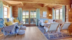 A cozy cabin interior with wooden walls, a dining area, and a seating area with ottomans and chairs.