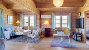 A cozy cabin interior with wooden walls, a dining area with a table and chairs, a sofa, and a television.