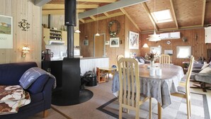 Interior acogedor de una cabaña con comedor, sala de estar con sofá y cocina con paredes de madera y chimenea.