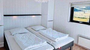 Une chambre avec deux lits, un luminaire suspendu, une fenêtre donnant sur un paysage agréable et un radiateur.