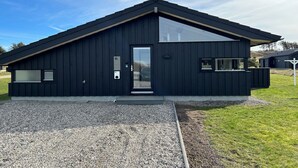 Un bâtiment moderne de couleur noire, doté d’un toit en pente, d’une grande porte vitrée et d’une allée gravillonnée.