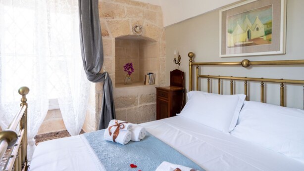 A hotel room with a bed, a stone fireplace, a painting, and a nightstand. - GuestHost - Comfortable apartment that hosts 2 people, located in an old farmhouse dating back to the 19th century, furnished with taste and meticulous recovery of the original materials. The accommodation is located in Cozzana, a quiet and verdant distr (Monopoli)