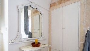 A white vanity with a mirror, a small table, and a white wardrobe. - GuestHost - Comfortable apartment that hosts 2 people, located in an old farmhouse dating back to the 19th century, furnished with taste and meticulous recovery of the original materials. The accommodation is located in Cozzana, a quiet and verdant distr (Monopoli)