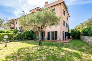 A two-story building with a garden and a tree in front.
