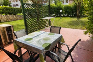 Um pátio externo com mesa e cadeiras, um cercado de treliça verde e uma parede de pedra.