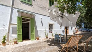 A building with a white facade, green shutters, a door, and a table with chairs outside. - GuestHost - Nice apartment that hosts up to 2 people, located in an old farmhouse dating back to the 19th century, furnished with taste and meticulous recovery of the original materials. The accommodation is located in Cozzana, a quiet and verdant distri (Monopoli)