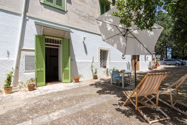 A building with a white facade, green shutters, a door, and a table with chairs outside.