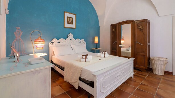 A bedroom with a bed, a wooden wardrobe, a nightstand, a lamp, and a framed picture on the wall. - GuestHost - Nice apartment that hosts up to 2 people, located in an old farmhouse dating back to the 19th century, furnished with taste and meticulous recovery of the original materials. The accommodation is located in Cozzana, a quiet and verdant distri (Monopoli)
