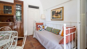 A bedroom with a bed, a white headboard, a painting on the wall, a wooden cabinet with glass doors, and a white table with chairs. - GuestHost - Nice apartment that hosts up to 2 people, located in an old farmhouse dating back to the 19th century, furnished with taste and meticulous recovery of the original materials. The accommodation is located in Cozzana, a quiet and verdant distri (Monopoli)