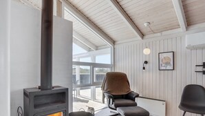 A modern room with a wood-burning stove, a comfortable chair, and a view through large windows.