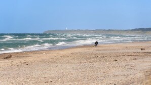A beach with a lighthouse in the distance and rough sea waves.
