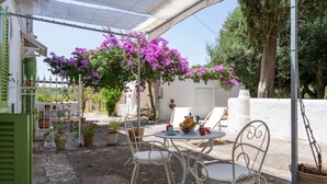 An outdoor patio with white metal chairs, a round table, and a pergola with purple bougainvillea flowers. - GuestHost - Lovely apartment that hosts up to 2 people, located in an old farmhouse dating back to the 19th century, furnished with taste and meticulous recovery of the original materials. The accommodation is located in Cozzana, a quiet and verdant dist (Monopoli)
