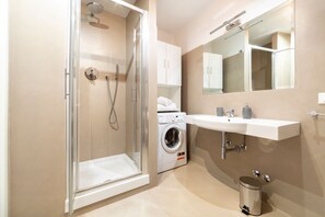 Een moderne badkamer met een douchecabine van glas, een ingebouwde wasmachine en een wastafel met spiegel.