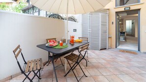 Une terrasse extérieure avec une table, des chaises, un grand parasol et une pile de chaises.