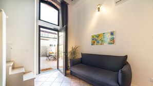 Un salon moderne avec un canapé foncé, un tableau accroché au mur et un escalier menant à un espace extérieur.