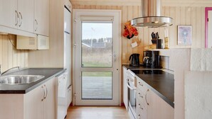Une cuisine moderne avec des meubles en bois, un évier en acier inoxydable et une vue sur l’extérieur grâce à une porte vitrée.