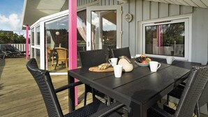 Un espace extérieur aménagé pour prendre les repas, avec une table, des chaises et une vue sur l’immeuble voisin.