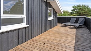 Ein modernes Gebäude mit dunkler Fassade, einer Holzterrasse und zwei Liegestühlen.