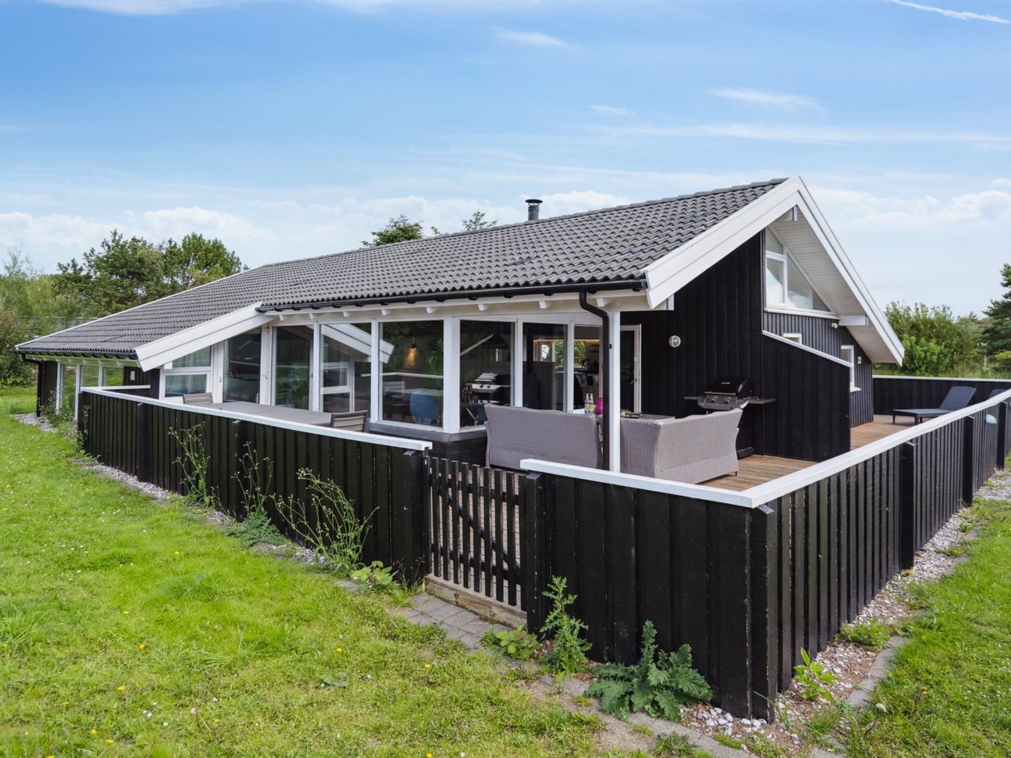 Ein modernes Haus mit überdachter Terrasse, großen Fenstern und schwarzem Anstrich.