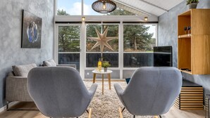 Ein modernes Wohnzimmer mit großem Fenster, grauen Sesseln, einer Couch und einer Holzkommode.