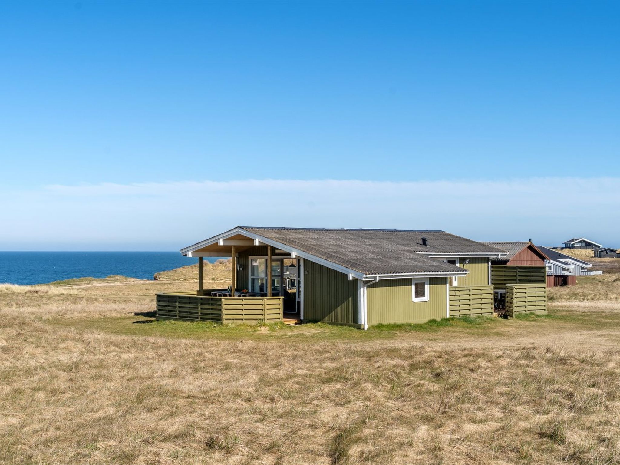 A small, single-story building with a porch, situated on a grassy field with a view of the ocean.