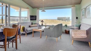 A spacious living room with a large window, a television, and a view of the beach.