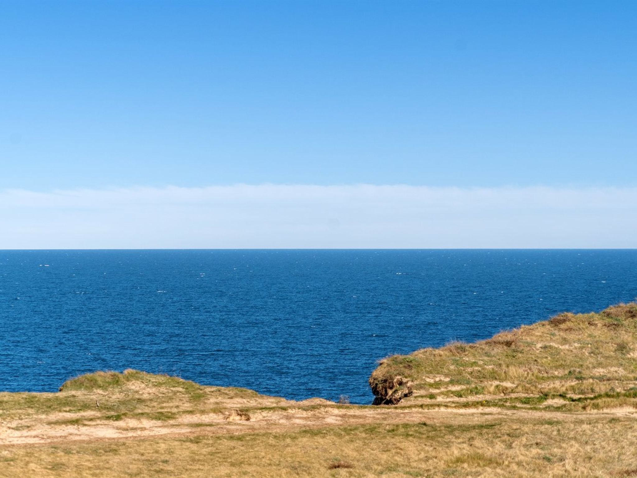 Un paysage côtier offrant une vue dégagée sur l’océan et une zone herbeuse avec une formation rocheuse.