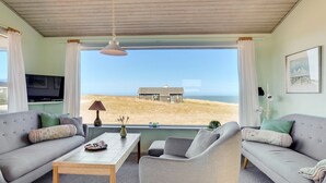 A living room with a view of the beach, a television, and a table with decorative items.