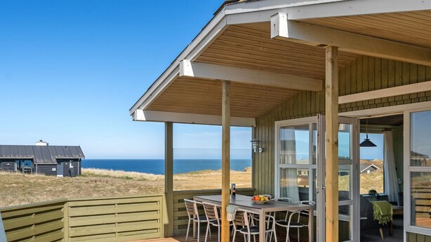 A wooden deck with a table and chairs, overlooking a beach and ocean.