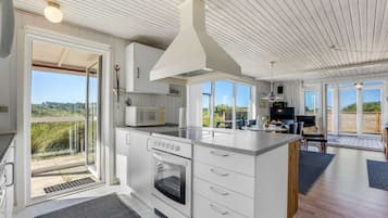 Une cuisine moderne dotée d’un grand îlot central, d’un four encastré et d’un four à micro-ondes. Une porte-fenêtre coulissante donne accès à un balcon offrant une vue sur la verdure.