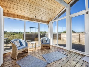 Une terrasse couverte, aménagée avec des meubles en osier, une petite table et offrant une vue sur l’extérieur.