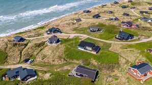Vista aérea de una zona residencial costera con casas, algunas con entradas y caminos visibles, y una playa al fondo.