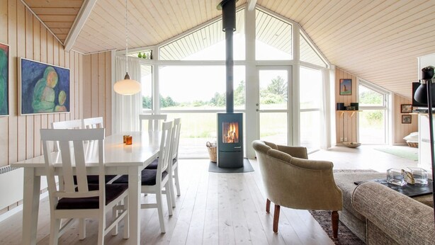 Een ruime woonkamer met een hoge nok, een open haard, witte meubels en grote ramen met uitzicht op de omgeving.