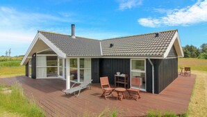 Een modern huis met een houten terras, grote ramen en een eethoek met tuinmeubilair.
