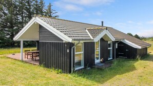 Een modern huis met een schuin dak, grote ramen en een overdekte veranda met stoelen.