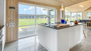 A modern kitchen with a large island, wooden ceiling, and large windows offering a view of the outdoors.