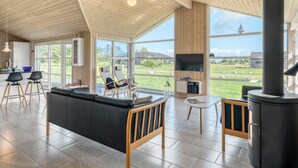 A spacious living area with a large black sofa, wooden chairs, a TV, and a fireplace.