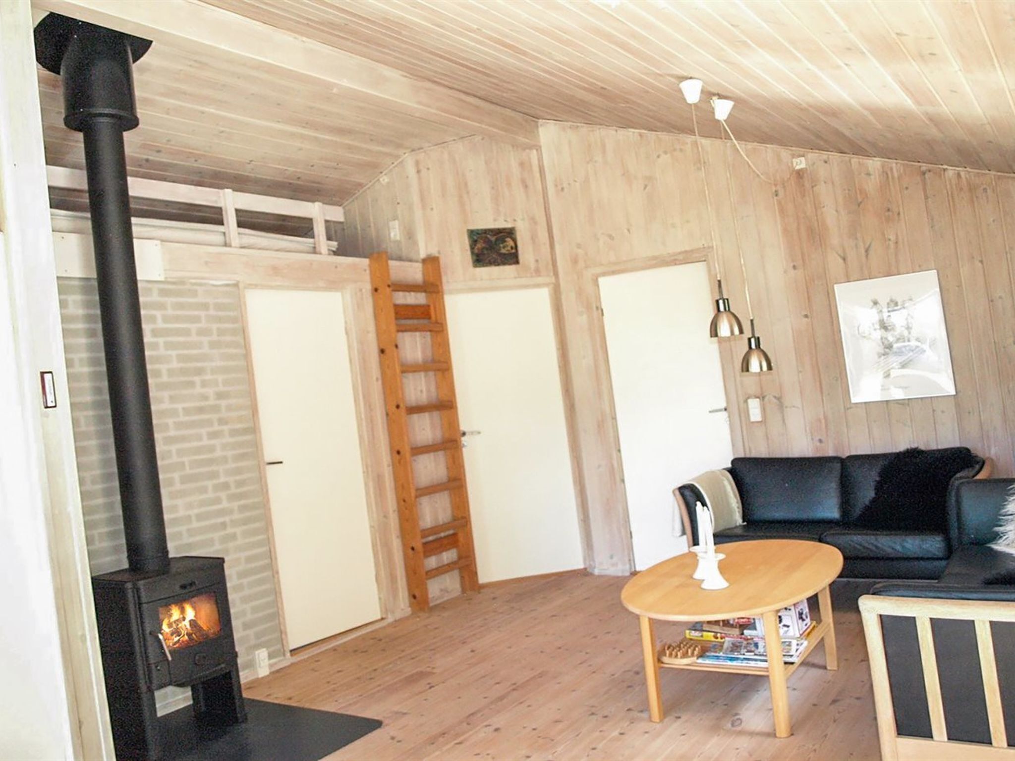 Een gezellige woonkamer met een houtkachel, een houten trap, een zwarte bank en een klein houten tafeltje.