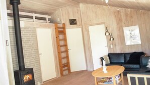 Una sala de estar acogedora con una estufa de leña, una escalera de madera, un sofá negro y una pequeña mesa de madera.