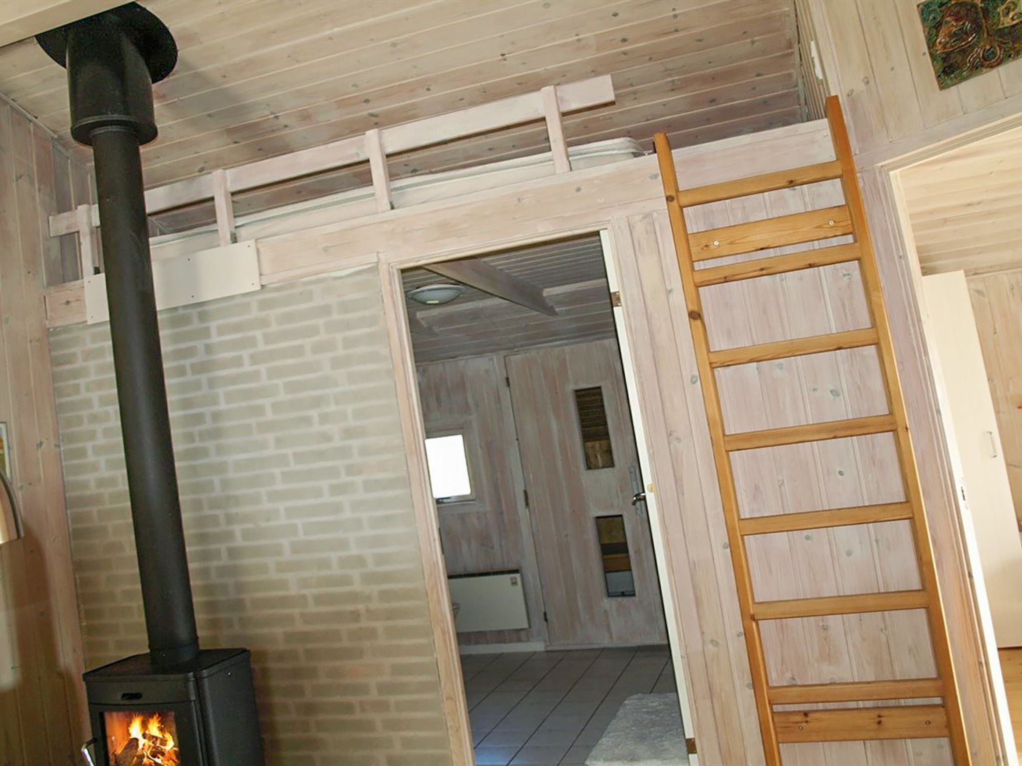 Une pièce avec un poêle à bois, une échelle en bois et une porte donnant sur une autre pièce.
