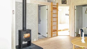 Una habitación con un estufa de leña negra, pisos de madera, una puerta blanca y una escalera de madera que da a un altillo.