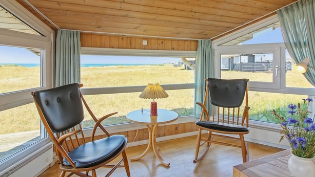 Een kamer met twee schommelstoelen gericht op een groot raam met uitzicht op een strand.
