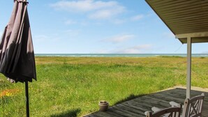Een houten terras met uitzicht op zee, een overdekt gedeelte met een bankje en een parasol.