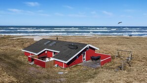 Een rood gebouw met een schuin dak en een klein terras, gelegen aan een strand met de oceaan op de achtergrond.